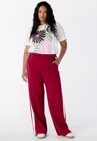 Witte t-shirt met bloemenprint in groen, roze en bordeaux. Loszittende bordeaux broek met zijsstripes en zakken. Gladde stof.