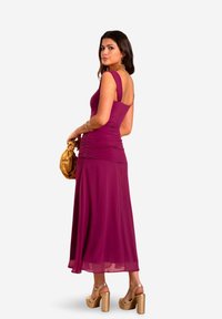 Fuchsia ärmelloses Kleid mit gerafften Details an der Taille, fließendem Rock und tiefem Rückenausschnitt. Kombiniert mit klobigen goldenen Absatzschuhen und einer goldenen Tasche.