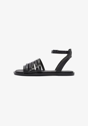 Sandal in pelle nera con ampie cinghie orizzontali, cinturino alla caviglia, suola piatta e design minimalista. Texture liscia e aspetto elegante.