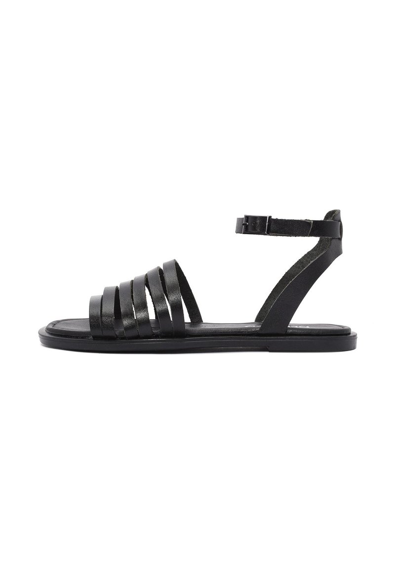 Sandal en cuir noir avec de larges sangles horizontales, une sangle de cheville, une semelle plate et un design minimaliste. Texture lisse et apparence épurée.