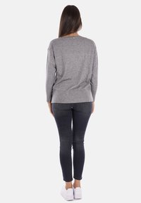 Top grigio a maniche lunghe con vestibilità rilassata, scollatura rotonda e spacchi laterali, abbinato a jeans skinny scuri e sneakers bianche.
