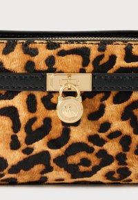 Leopardų užpildyto maišelio, pagaminto iš struktūrinės sintetinės medžiagos. Juodos odos akcentai ir auksinės spalvos užrakto detalė su logotipu. Užtrauktuko uždarymas viršuje.