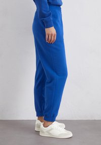Blauwe katoenen joggingbroek met een elastische tailleband en boorden. Gecombineerd met witte sneakers, voorzien van grijze accenten aan de zijkanten.