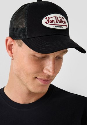Black trucker cap with mesh sides, featuring a white oval patch with "Von Dutch" in red font and "ORIGINAL" in black beneath.