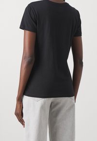 Czarna bawełniana koszulka z krótkim rękawem, okrągłym dekoltem i dopasowanym krojem, połączona z jasnoszarymi szerokimi spodniami.