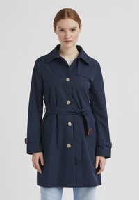 Dunkelblauer Trenchcoat aus glattem Stoff, mit Kragen, goldenen Knöpfen und einem abnehmbaren Gürtel mit braunen Lederakzenten.