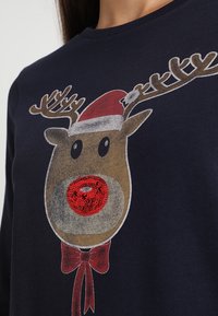 Tmavě modrá mikina s grafikou soba se červeným nosem, hnědými parohy a čepicí Santa Clausa, doplněná designem červeného motýlku.