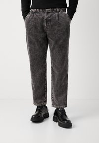 Zwart-grijze gestreepte corduroybroek met een relaxed fit, voorzien van plooien, zijzakken, en gedragen met zwarte veterschoenen.