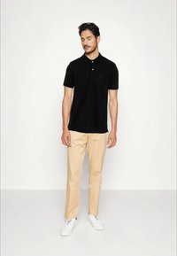 Svart polo skjorta med tre-knapplås, bärs med beige byxor. Tillsammans med vita sneakers har outfiten en avslappnad passform.