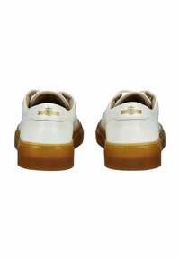 Białe skórzane sneakersy z beżową gumową podeszwą, z złotym emblematem na pięcie i gładkim, zaokrąglonym kształtem.