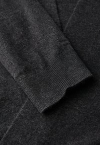 Grauer Strickpulloverstoff mit sichtbarer Textur, der über ein geripptes Bündchen und eine weiche, flauschige Oberfläche verfügt. Eine Nahaufnahme hebt die Materialdetails hervor.
