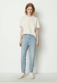 Light blue jeans, tapered fit, with a faded wash and minimal stitching details. Paired with a plain white short-sleeve t-shirt and white sneakers.