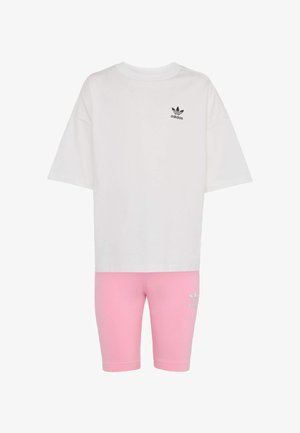 Bijela pamučna majica kratkih rukava s crnim Adidas logotipom, uparena s ružičastim elastičnim kratkim hlačama koje imaju isti logotip na bedru.