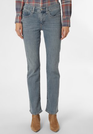 Personne portant un jean bleu délavé droit, des bottines en daim marron et une chemise rouge et grise à carreaux à manches longues, debout.