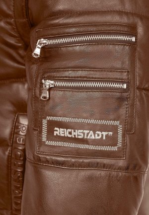 Pantaloni in pelle marrone con multiple tasche con zip e un'etichetta del brand cucita che recita "REICHSTADT." Texture liscia con sottili dettagli a grana.