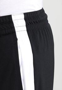 Schwarze Sportshorts mit einem weißen Seitenstreifen, ausgestattet mit einem elastischen Taillenbund und glatter Textur. Keine sichtbaren Taschen.
