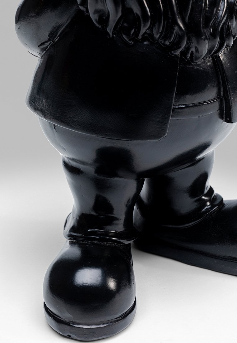 Figurine noir brillant aux proportions exagérées, portant un costume, avec un derrière saillant, de courtes jambes et de distincts bottes brillantes.
