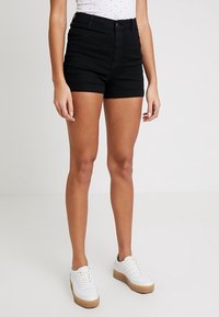 Shorts en denim noir à taille haute, ourlet retroussé et poches avant, assortis à des baskets blanches avec une semelle texturée.