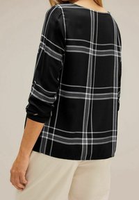 Top a scacchi neri con maniche lunghe, caratterizzato da un motivo a quadri bianchi. Tessuto morbido con una vestibilità leggermente ampia e scollo a barchetta.