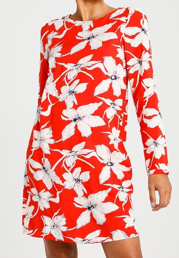 Robe fleurie rouge à manches longues, ornée de grandes fleurs blanches avec des accents noirs. Tissu lisse et léger, encolure ronde, longueur au-dessus du genou.