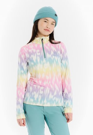 Jonge vrouw draagt een pastel multicolor lange mouw trui en teal broek, met een lichtblauwe gebreide muts.