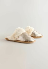 Glittery gold slippers with a soft, white faux fur cuff, round toe, and a tan rubber sole. The upper features a sparkly texture.