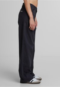 Pantalones de pierna ancha azul marino oscuro hechos de algodón con un acabado ligeramente texturizado. Presentan un bolsillo trasero y un bordado sutil del logotipo.