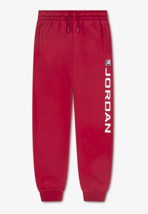 Czerwone spodnie dresowe z elastycznym pasem, bocznymi kieszeniami i ściągaczami na końcach nogawek. Z białym napisem "JORDAN" wzdłuż lewej strony oraz naszywką z logo.