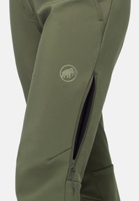 Pantalons softshell verts avec poches zippées, une coupe ajustée, des détails cousus et un logo circulaire représentant un éléphant.