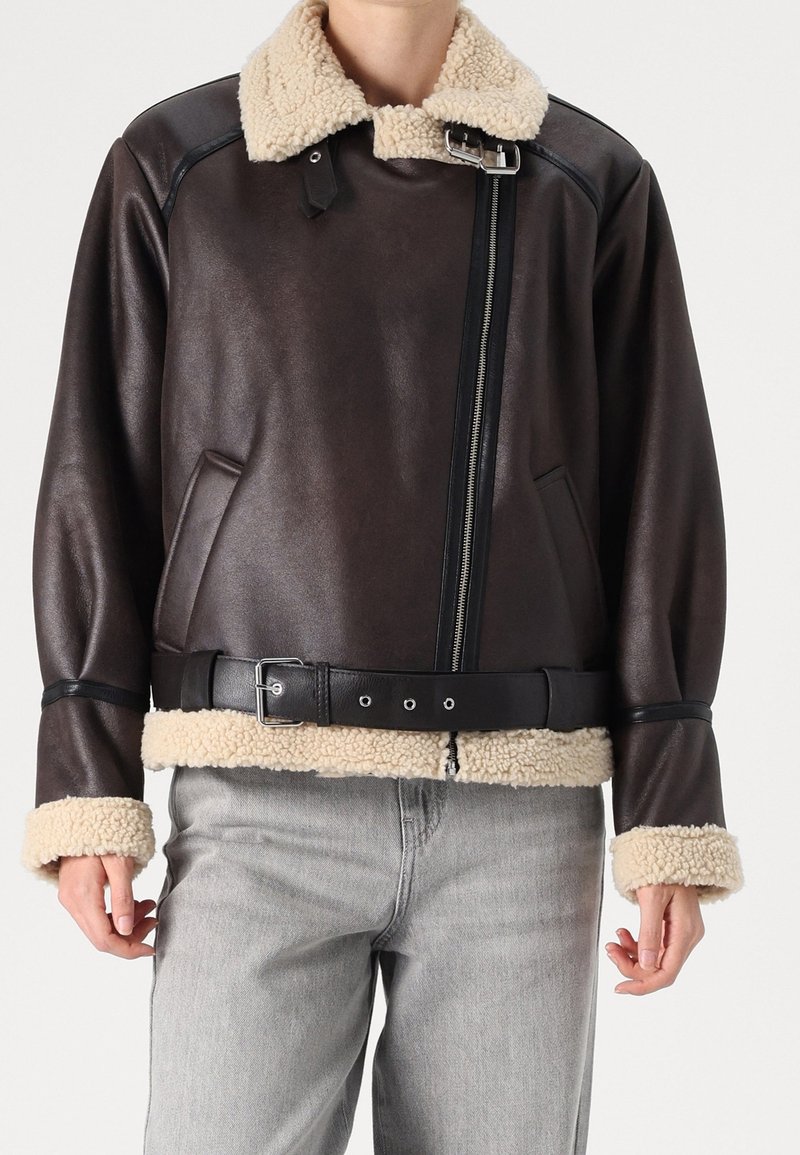 Veste en cuir marron avec col et poignets en shearling, dotée d'une fermeture éclair diagonale et d'une ceinture noire avec des boucles en métal argenté.