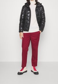 Personne portant une doudoune noire brillante, un col roulé blanc, un pantalon rouge foncé et des baskets montantes blanches avec des lacets rouges.