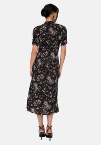 Black floral dress with short puff sleeves, a fitted waist, and a midi length. Features cream floral patterns and a split hem. Black heeled sandals.