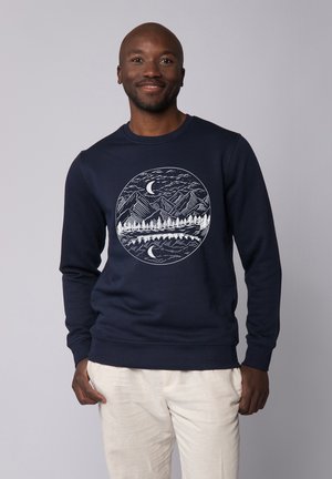 Marineblauwe sweatshirt met een cirkelvormige witte graphic van bergen, bomen en een waterlichaam, met een halve maan en een gestructureerde stof.