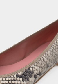 Γυναικείο παπούτσι μπαλαρίνα με εξωτερική επιφάνεια σε μοτίβο δέρματος φιδιού σε μπεζ και μαύρες αποχρώσεις και ροζ εσωτερική επένδυση, σε λευκό φόντο.