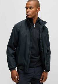 Schwarze leichte Jacke mit Stehkragen, Reißverschluss und elastischen Bündchen. Verfügt über eine glatte Textur und ein schlankes Design, das sich gut zum Layering eignet.