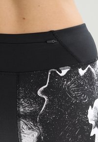 Leggings neri con un motivo testurizzato che presenta disegni astratti bianchi. Vita alta con una piccola tasca con zip sul retro.