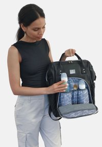 Zaino da viaggio per pannolini nero con molteplici scomparti, con un interno foderato in grigio, che contiene biberon e un cucchiaio nella tasca frontale.