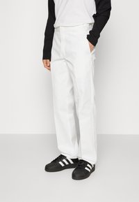 White straight-leg pants made of smooth fabric, featuring side pockets. Paired with black sneakers with white stripes.