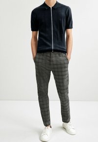 Polo tricot à manches courtes marine avec des rayures verticales texturées ; associé à un pantalon à carreaux gris avec une coupe ajustée et des baskets blanches.