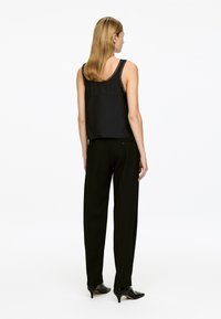 Black sleeveless top with lace trim, paired with black tailored trousers and pointed black heels, viewed from the back.