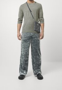 Graues langärmliges Strickshirt mit Schulterdetails, kombiniert mit grauen Samt-Hosen in weiter Form. Eine kleine Handtasche mit Muster rundet das Outfit ab.
