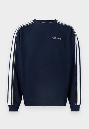 Μπλε ναυτικό φούτερ Calvin Klein με λευκές και κίτρινες ρίγες κατά μήκος των μανικιών και μικρό λευκό λογότυπο στο επάνω αριστερό μέρος του στήθους.