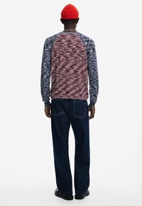 Pikad varrukad ja mitmevärviline, tekstuuriga muster; sinised varrukad; ühendatud tumesiniste teksapükste ja mustade jalatsitega.