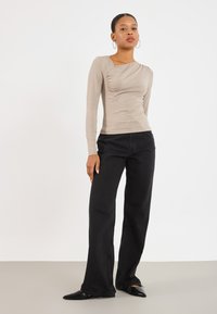 Top a maniche lunghe beige con dettagli arricciati; abbinato a jeans neri a gamba larga e ballerine nere con punta. Design semplice e aderente in tutto.