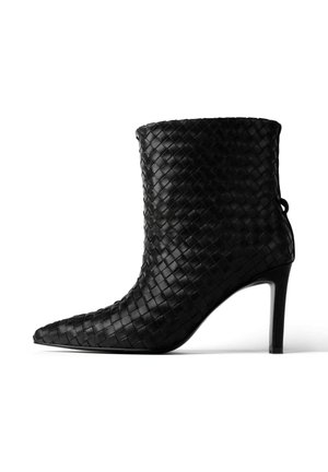 Czarny, pleciony skórzany botek za kostkę z wąskim noskiem i cienkim obcasem w kształcie szpilki. Posiada teksturowaną powierzchnię oraz pętelkę z tyłu.
