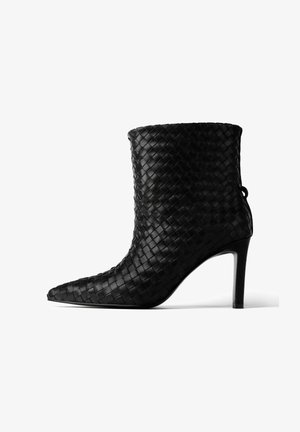 Czarny, pleciony skórzany botek za kostkę z wąskim noskiem i cienkim obcasem w kształcie szpilki. Posiada teksturowaną powierzchnię oraz pętelkę z tyłu.