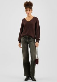 Bordowy sweter z dzianiny z dekoltem w serek, z oversized rękawami, w połączeniu z ciemnozielonymi szerokimi spodniami i czarnymi botkami za kostkę. Srebrna torebka na łańcuszku.