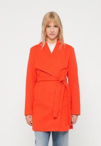 Casaco envolto laranja com cinto, mangas longas, colarinho com cortes, bolsos frontais e um design até ao joelho, feito de um tecido macio e texturizado.