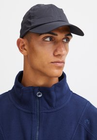 Giacca in fleece blu navy con colletto alto, abbinata a un cappello grigio scuro con visiera curvata e dettagli di cucitura visibili.