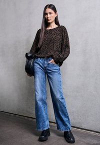 Camicia a maniche lunghe con stampa leopardata marrone abbinata a jeans a gamba larga azzurri e stivaletti neri a zeppa. Il modello tiene una borsa nera.